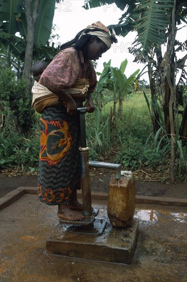 TANZANIA, West, Great Lakes Region, Woman with baby tied on her back collecting water from pump in refugee camp.