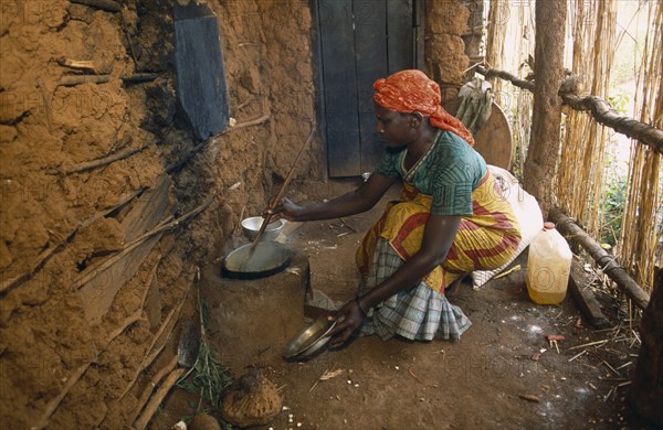 TANZANIA, West, Great Lakes Region, Refugee woman cooking on wood saving clay stove inside hut with mud brick walls.