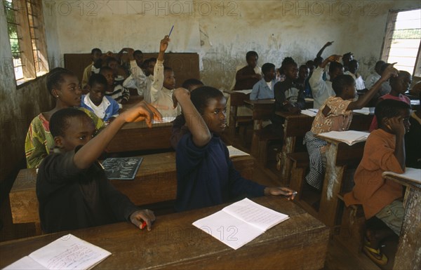 TANZANIA, West, Great Lakes Region, School for refugee children in Great Lakes camp.  Children at desks in classroom with raised hands.