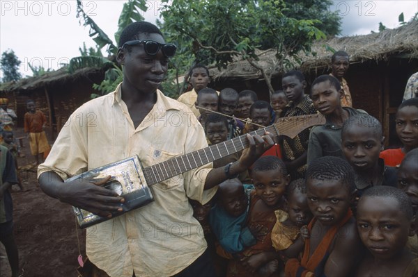 TANZANIA, West, Great Lakes Region, Refugee children listening to boy playing guitar made from cooking oil can.