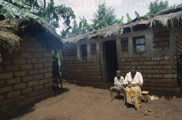 TANZANIA, West, Great Lakes Region, "Refugee woman and child sitting outside thatched, mud brick home in camp."