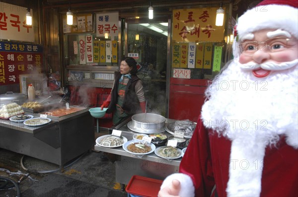 KOREA, Seoul , Namdaemun Market in December. Streetside restaurant with Santa Claus outside and a woman cook in the background