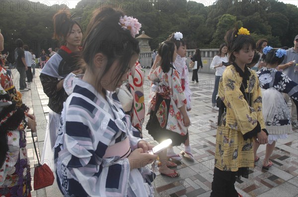 JAPAN, Honshu, Tokyo, Harajuku. A member of Kyoto Rokumeikan troupe checks her mobile / cell phone during a break from dancing at Yoyogi Park dressed in half kimono costume on Saturday afternoon