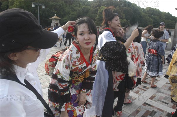JAPAN, Honshu, Tokyo, Harajuku. A member of the Kyoto Rokumeikan troupe has her hair adjusted during a break from dancing at the entrance of Yoyogi Park dressed in half kimono costumes on Saturday afternoon