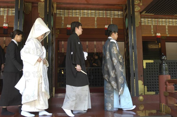 JAPAN, Honshu, Tokyo, Nezu. Shinto priest leads newly married couple out of Nezu Jinja shrine after Shinto ceremony with bride and groom in traditional costume