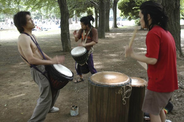 JAPAN, Honshu, Tokyo, "Harajuku. Yoyogi Park. Hiroaki Komura  and his brother Kenichi, with their friend Tomokazu Nagashima, playing African drums on a Saturday afternoon"