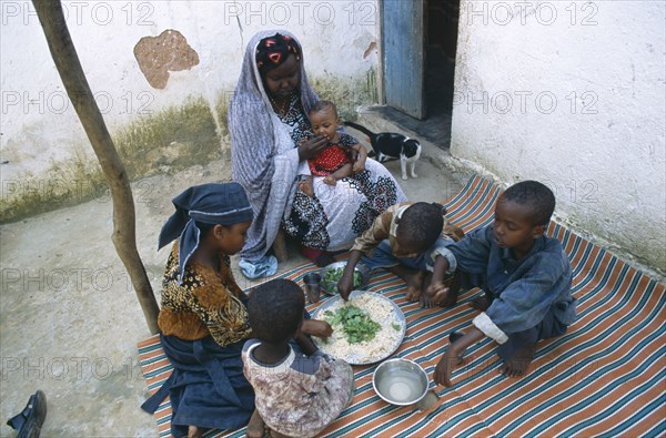 SOMALIA, Baidoa, Woman and children eating lunch from communal dish using the right hand.  At a family meal men are usually served first and women and children eat seperately later.