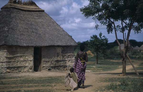 SOMALIA, Tribal People, Woman and child walking towards traditional thatchedhouse near Baidoa.