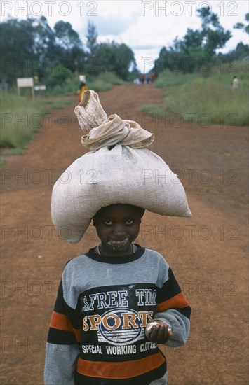 TANZANIA, West, Great Lakes Region, Young refugee girl carrying sack of food on her head with remnants of food all around her mouth.