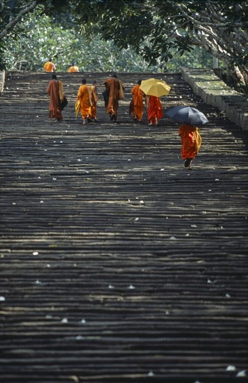 SRI LANKA, Mihintale, Monks climbing the steep pathway carrying umbrellas to shade themselves from the sun.