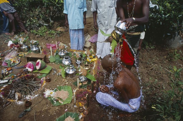 SRI LANKA, Haputale, Funeral ritual with son of the deceased with head shaved as sign of bereavement having water poured over him while sitting on ground beside fire and offerings.