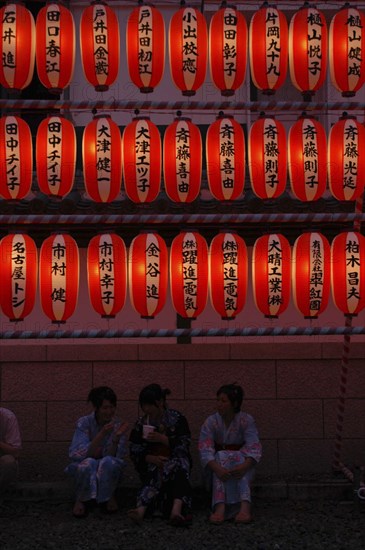 JAPAN, Chiba, Narita, "Teenage girls in yukata, summer kimono, sit beneath chochin lanterns each with the name of a donor to Narita san Temple during Gion Matsuri"