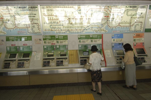 JAPAN, Honshu, Tokyo, Ueno train station with women buying train tickets from vending machines with the train route map above