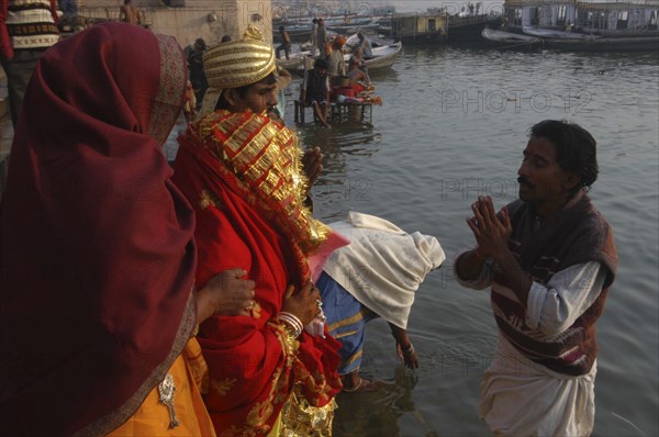 INDIA, Uttar Pradesh, Varanasi , Bhramin pundit or priest stands in the Ganges River at Dashaswamedh Ghat and conducts a prayer for a bride and groom