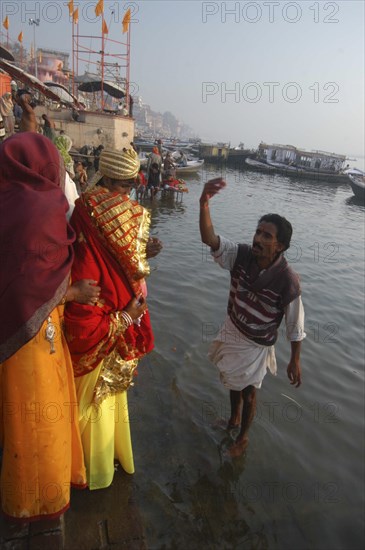 INDIA, Uttar Pradesh, Varanasi , Bhramin pundit or priest at Dashaswamedh Ghat stands in the Ganges River and flicks water in blessing over a bride and groom