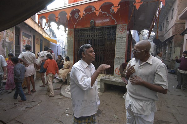 INDIA, Uttar Pradesh, Varanasi , Bengali Tole. Two middle aged men have a morning coversation outside a temple using their hands to stress the points they are making