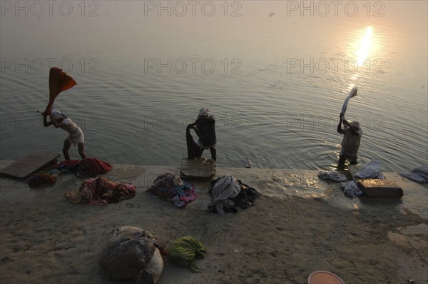 INDIA, Uttar Pradesh, Varanasi , Near Shivala Ghat. Dhobi clothes washers working on the banks of the Ganges River with low sun on the horizon