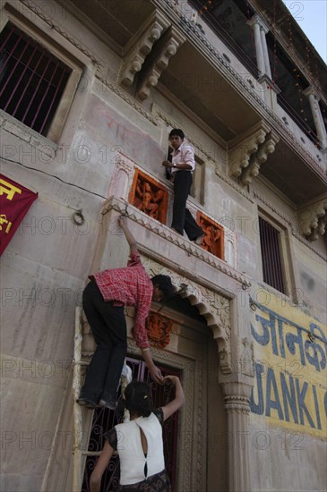 INDIA, Uttar Pradesh, Varanasi , Deep Diwali Festival with teenage boys climbing a doorway to decorate Hindu shrine