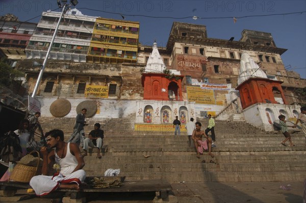 INDIA, Uttar Pradesh, Varanasi, Dasashwamedh Ghat. View looking up at a temple and the houses behind the ghats with a Hindu Bhramin pundit sitting waiting for his next customer on the steps
