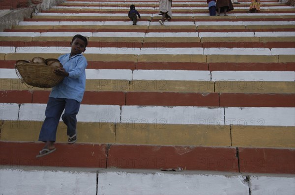 INDIA, Uttar Pradesh, Varanasi, Boy carrying basket down steps to a ghat on the Ganges River