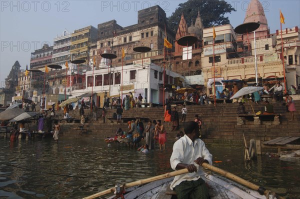 INDIA, Uttar Pradesh, Varanasi, A boatman bringing his boat into Dashaswamedh Ghat with early morning bathers in the Ganges River