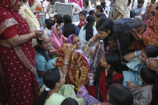 INDIA, Uttar Pradesh, Varanasi, Sankat Mochan Mandir temple. Women friends and relatives cheer a bride with her head draped in a red sari at her wedding outside the temple