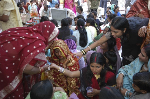 INDIA, Uttar Pradesh, Varanasi, Sankat Mochan Mandir temple. Women friends and relatives comfort and cheer a bride in a red and gold sari at her wedding outside the temple