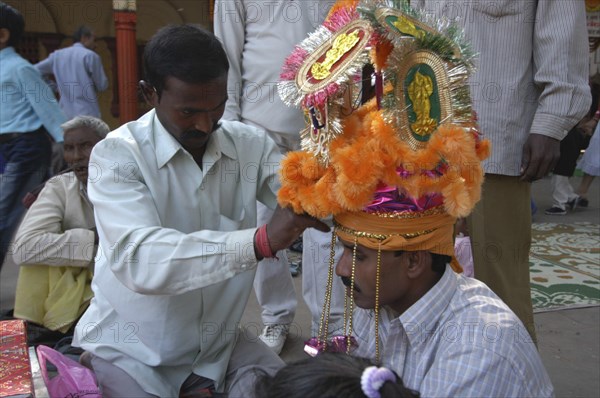 INDIA, Uttar Pradesh, Varanasi, Sankat Mochan Mandir temple. A groom having his headdress / hat adjusted at his wedding outside the temple