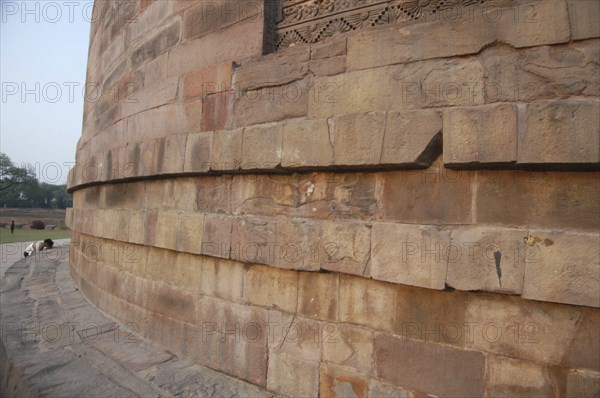 INDIA, Uttar Pradesh, Sarnath, Dhamek Stupa with a Buddhist pilgrim kneeling in prayer at the base