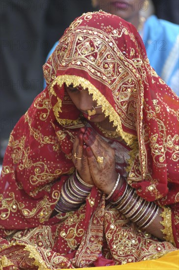 INDIA, Uttar Pradesh, Varanasi, Sankat Mochan Mandir temple. Hindu bride dressed in red and gold sari with her hands in namaste gesture painted with henna design and wearing glass bracelets