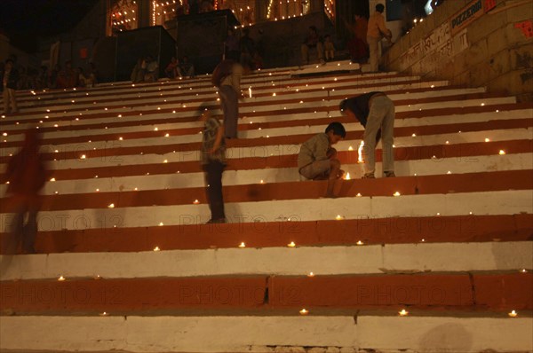 INDIA, Uttar Pradesh, Varanasi, Deep Diwali Festival with young boys lighting oil lamps on steps leading down to the Ganges River