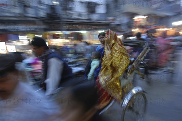 INDIA, Uttar Pradesh, Varanasi, The Godaulia intersection. A passing rickshaw with two women in saris in the evening. Movement blur.