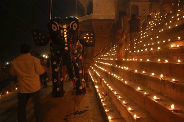INDIA, Uttar Pradesh, Varanasi, Deep Diwali Festival with paper statue of Hindu God Ganesh on steps of ghats lined with oil lamps leading to Ganges River