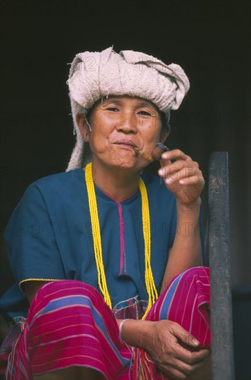 THAILAND, Chiang Mai, Doi Inthanon National Park. Portrait of a Karen woman sitting on the steps of her house smoking a pipe