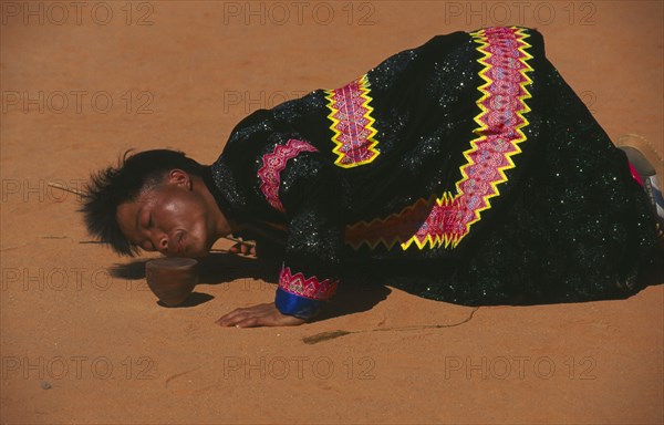 THAILAND, Chiang Mai, Hmong man blowing stones out of the way of his spinning top at Hmong New Year festival