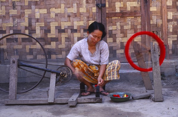 MYANMAR, Kachin State, Myitkyina, Jinghpaw woman spinning thread onto a bobbin for weaving at a weavers shop
