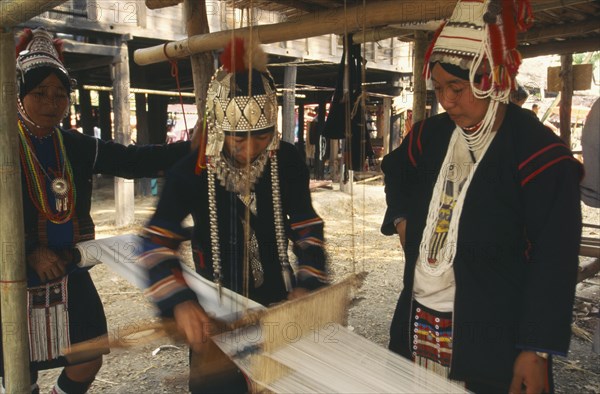 THAILAND, Chiang Mai, Akha woman weaving cloth on an Akha loom as other women look on