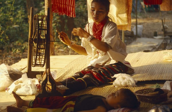 THAILAND, Chiang Mai Province, Lawa woman spinning thread inside her house with her young son lying in the foreground