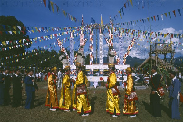 THAILAND, Chiang Mai, Samathi Mai, Kachin Manou Dance leaders passing Manou posts in the background