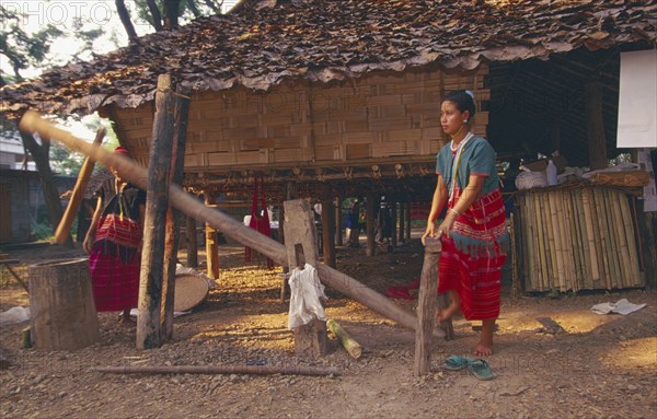 THAILAND, Chiang Mai, Sgaw Karen woman using a foot powered rice pounder to remove husks