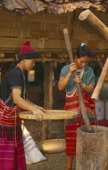 THAILAND, Chiang Mai, Sgaw Karen woman pounding rice by hand while another sifts with a large bamboo tray