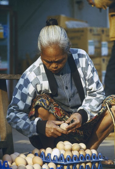 LAOS, Luang Prabang, Elderly woman selecting eggs to purchase at the morning market