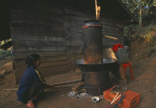 THAILAND, Chiang Rai Province, Doi Lan, Lisu woman stoking fire of her still for making corn whiskey