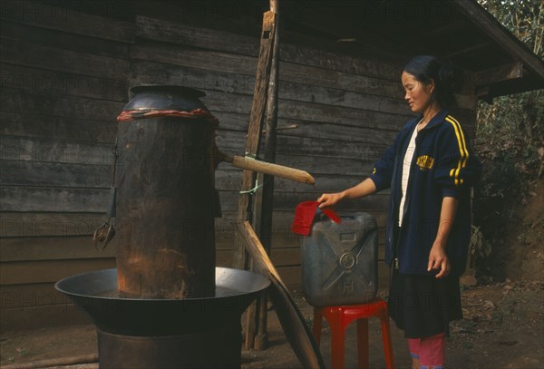 THAILAND, Chiang Rai Province, Doi Lan, Lisu woman checking cloth filter on the spout of her still for making corn whiskey