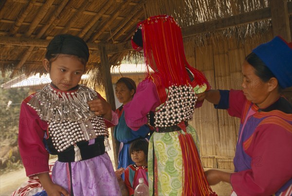 THAILAND, Chiang Rai Province, Huai Khrai, Young Lisu girls dressed in their New Year finery while their mother adjusts their vests