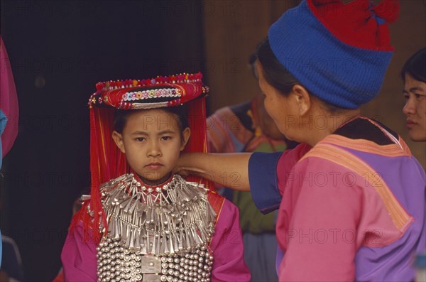 THAILAND, Chiang Rai Province, Huai Khrai, Young Lisu girl dressed in her New Year finery while her mother adjusts her silver neck chain
