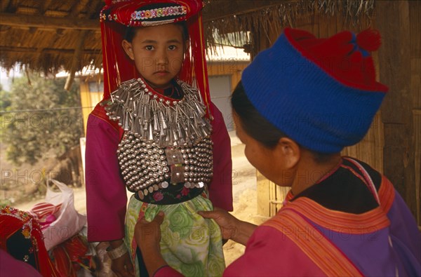 THAILAND, Chiang Rai Province, Huai Khrai, Young Lisu girl dressed in her New Year finery while her mother adjusts her tunic