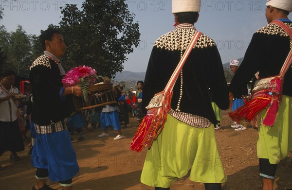 THAILAND, Chiang Rai Province, Huai Khrai, Lisu man carrying offerings to put by the New Year tree surrounded by dancers