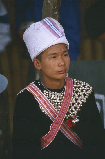 THAILAND, Chiang Rai Province, Doi Lan, Young Lisu man at New Year dance wearing his New Year studded jacket and white towel turban