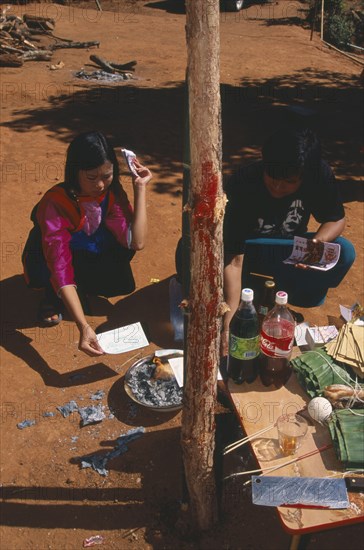 THAILAND, Chiang Mai Province, Bahn Mae Phaem, Lisu girl and man burning imitation money beside New Year tree with chicken blood on the trunk